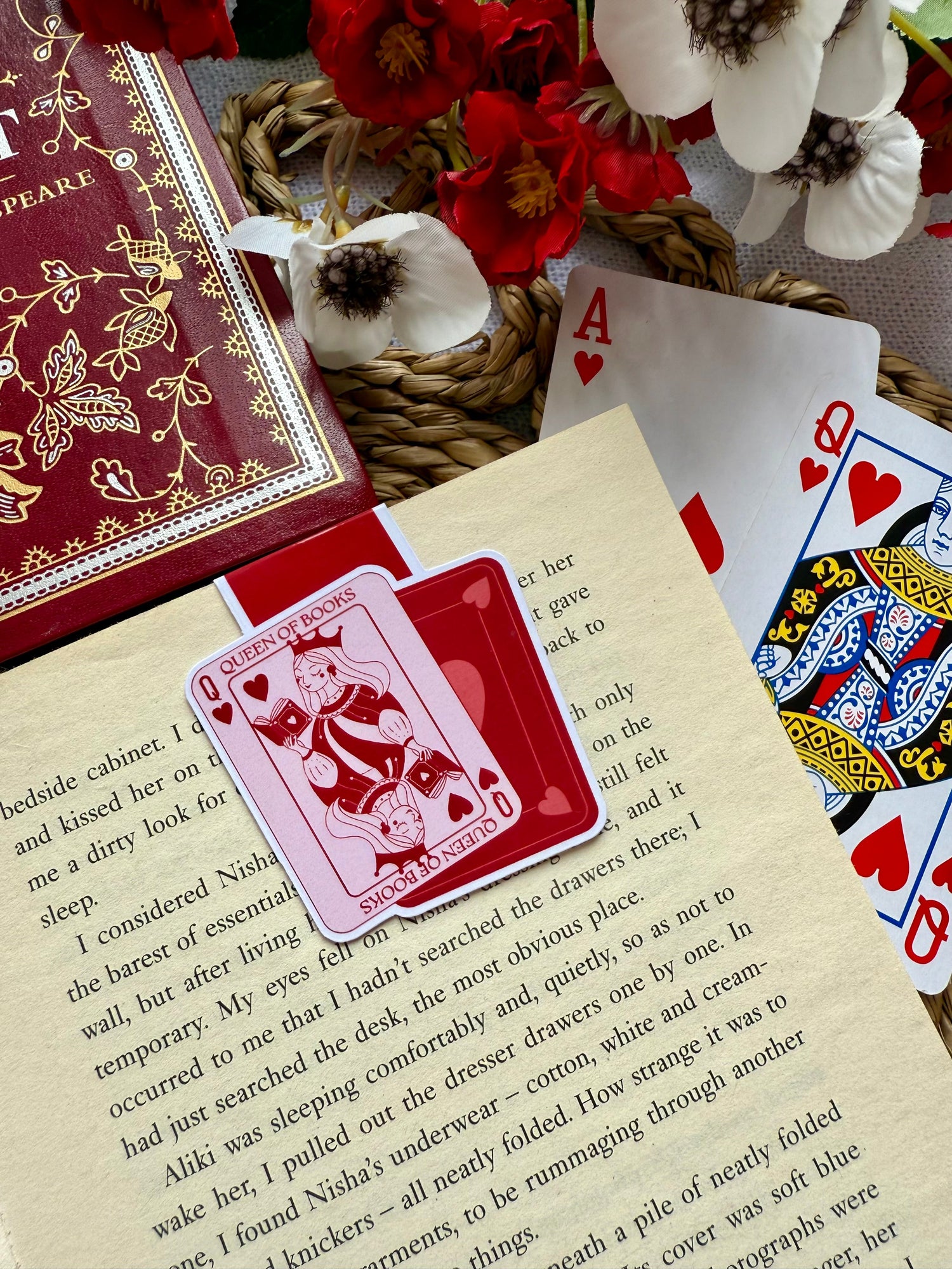 A magnetic bookmark of playing cards showing queens with the words queen of books. The magnetic bookmark is placed on the page of an open book.