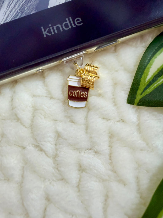 Gold coffee cup and book charm on a white textured surface with a Kindle device in the background.