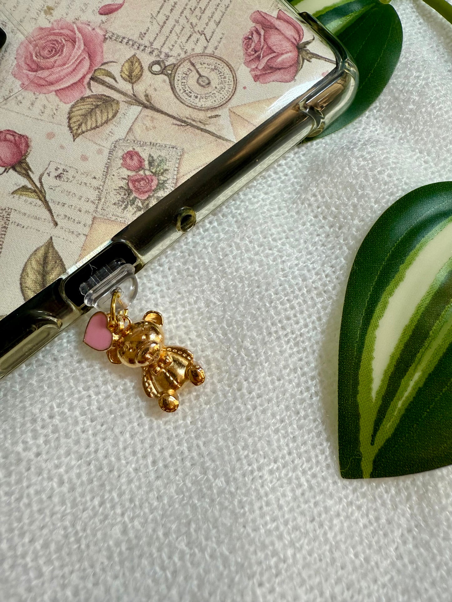An e-reader charm of a gold teddy and a pink heart attached to a kindle 