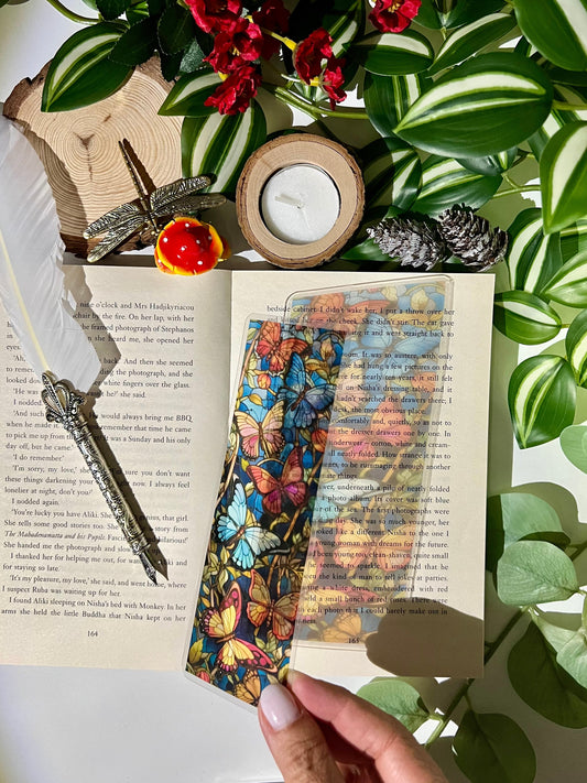 Colorful transparent stained glass butterfly bookmark on an open book with decorative elements and plants.