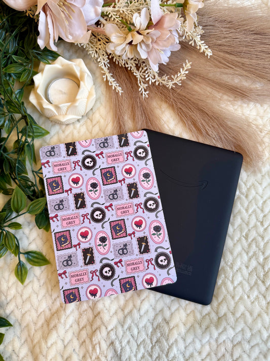 A black Kindle e-reader with a decorative dark romance patterned cover lying on a cream knit blanket, styled with dried flowers, greenery, and a candle.