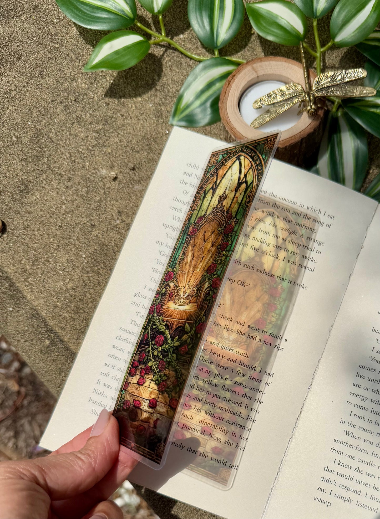 A stained glass bookmark of a throne with red roses. The bookmark is placed over an open book allowing the sunlight to reflect the image of the bookmark onto the book