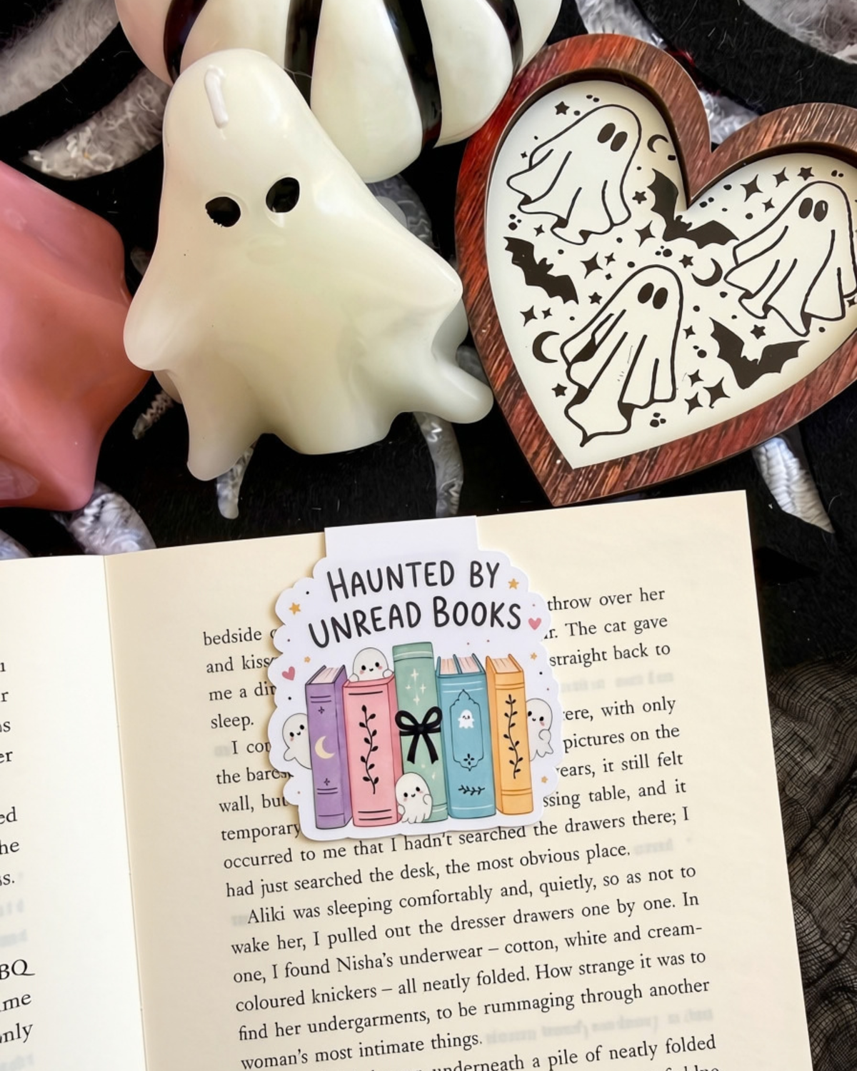 A Halloween-themed magnetic bookmark featuring a 'Haunted by Unread Books' design, displayed on an open book with ghost-shaped candles and a wooden heart-shaped tray decorated with ghost illustrations.