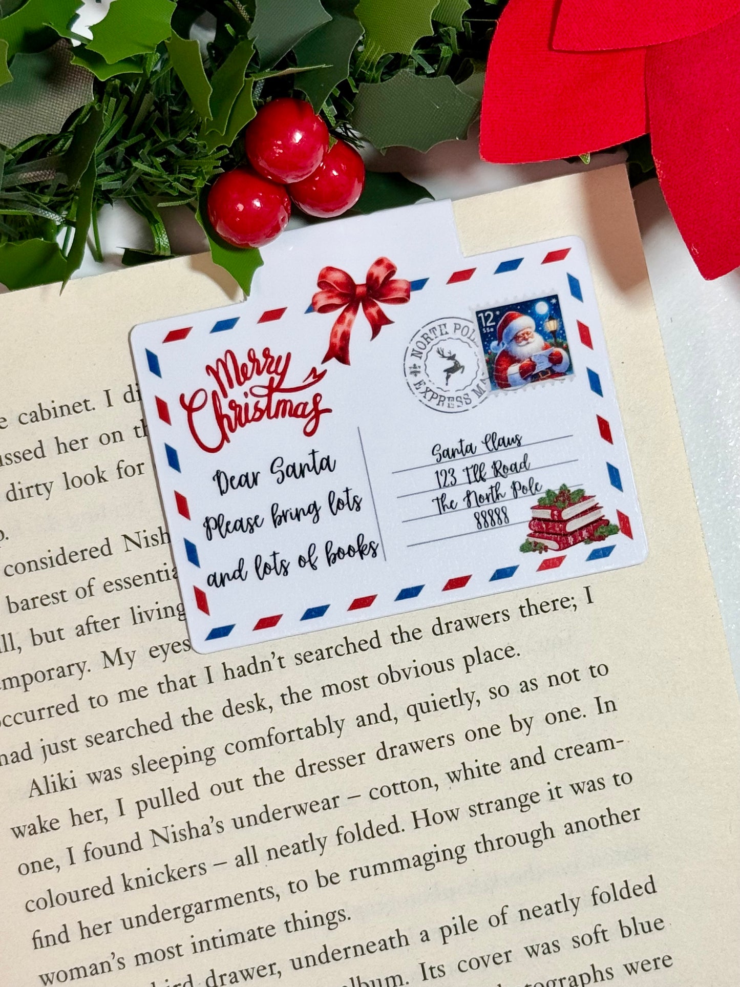 A magnetic bookmark of a postcard to Santa. The bookmark is placed on an open book with Christmas decorations.