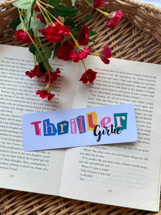 Colorful 'Thrille Girlie' bookmark on an open book with red flowers.