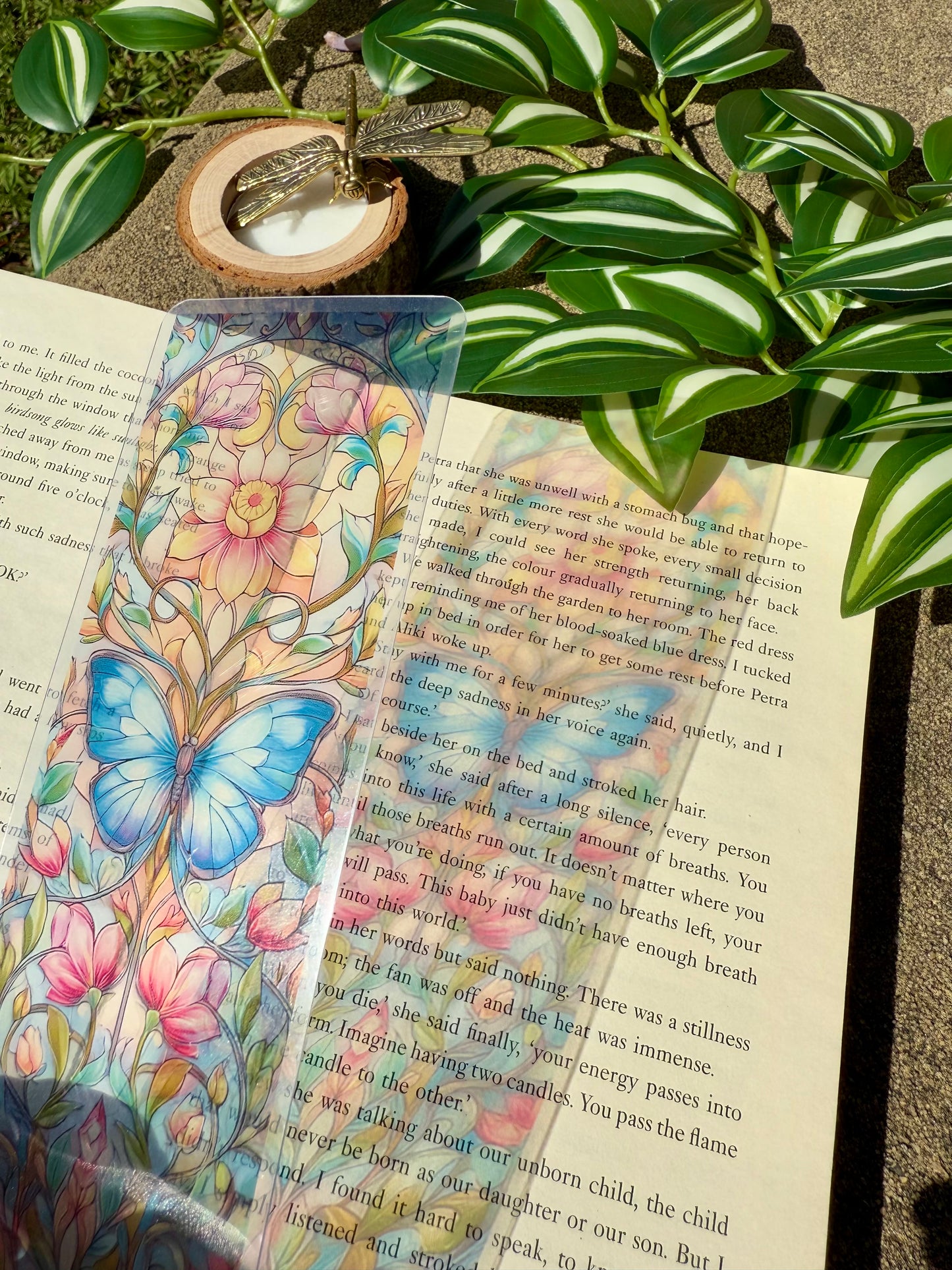 Colorful butterfly and floral stained glass bookmark on an open book with green leaves in the background