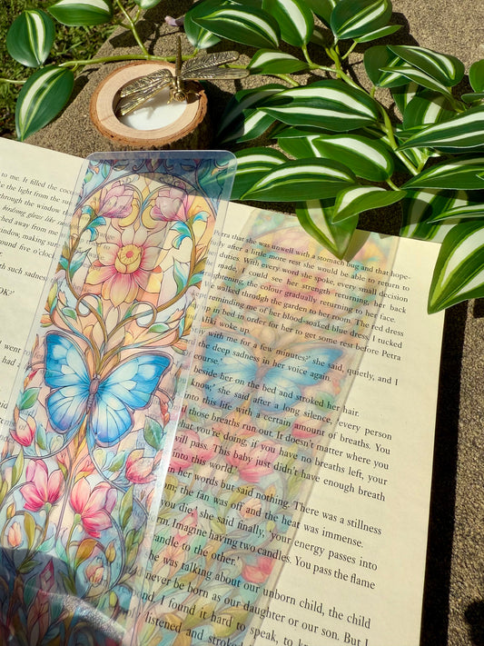 Colorful butterfly and floral stained glass bookmark on an open book with green leaves in the background