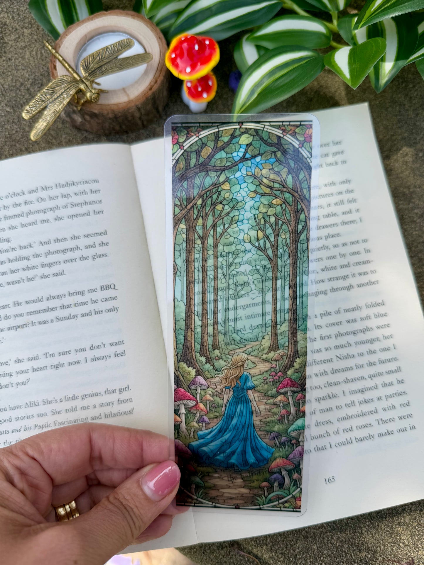 A stained glass bookmark of a girl walking through a forest with mushrooms growing along the path