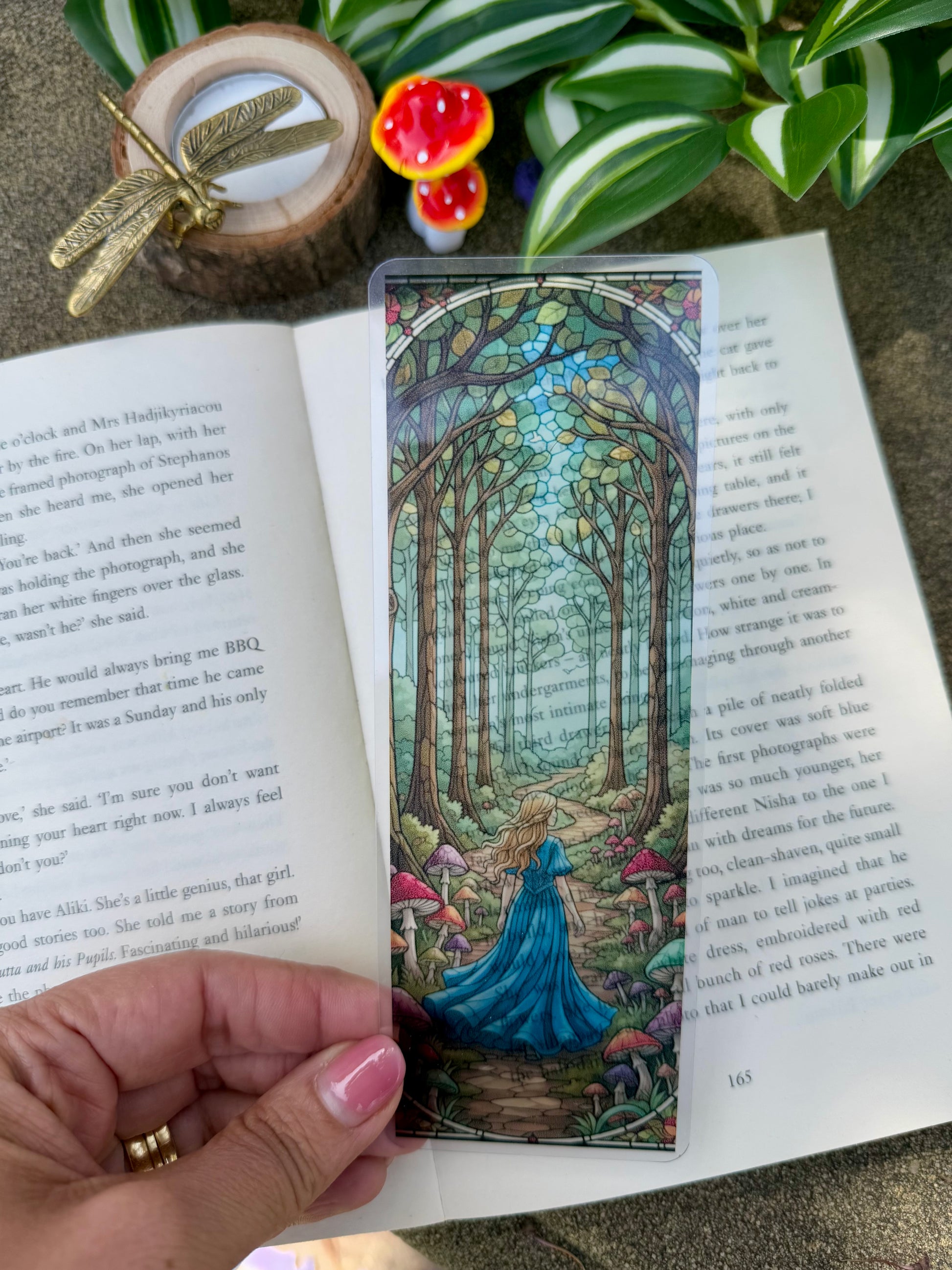 A stained glass bookmark of a girl walking through a forest with mushrooms growing along the path