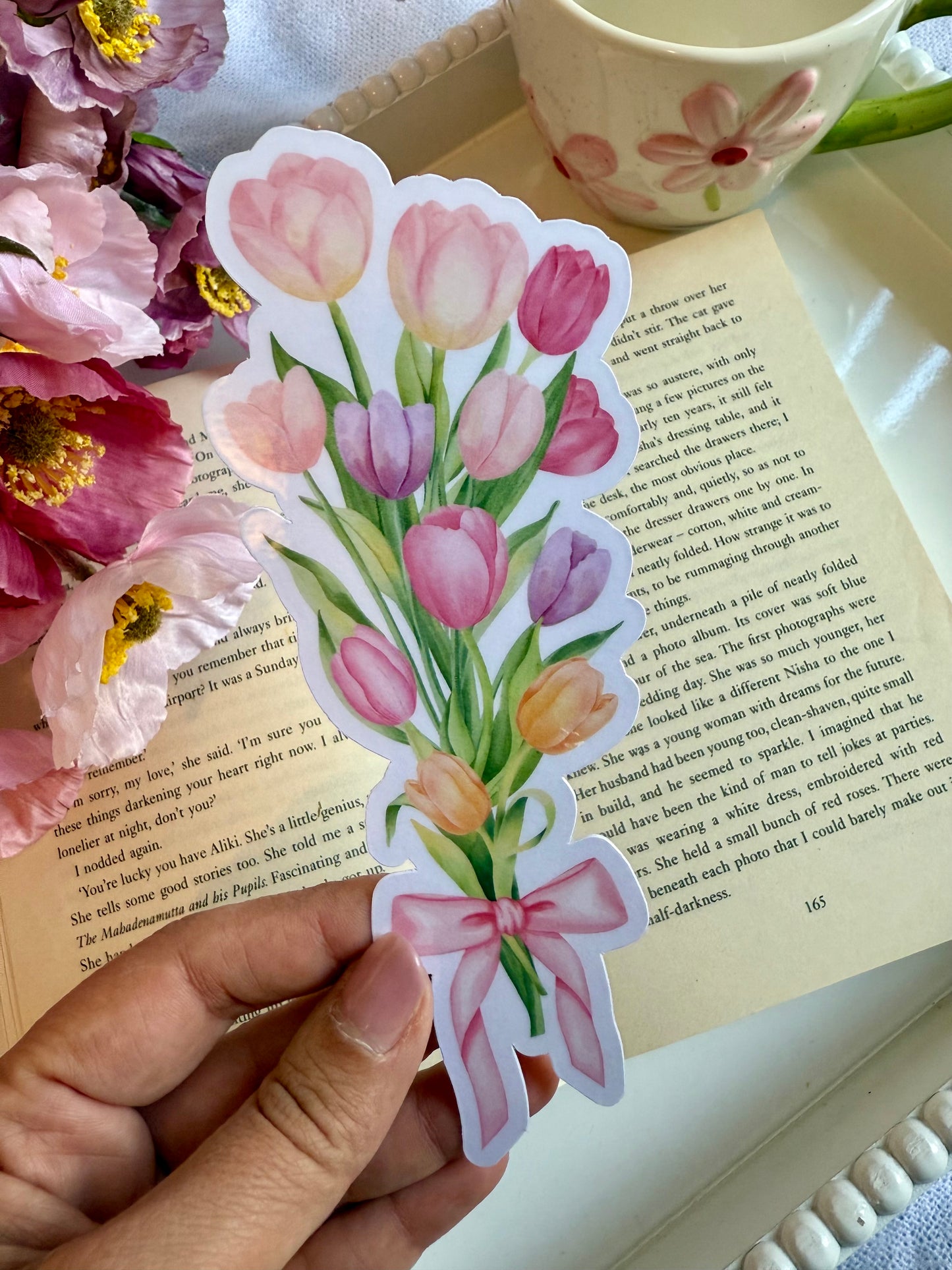 A die cut bookmark of a bouquet of tulips. The bookmark is held over an open page of a book.