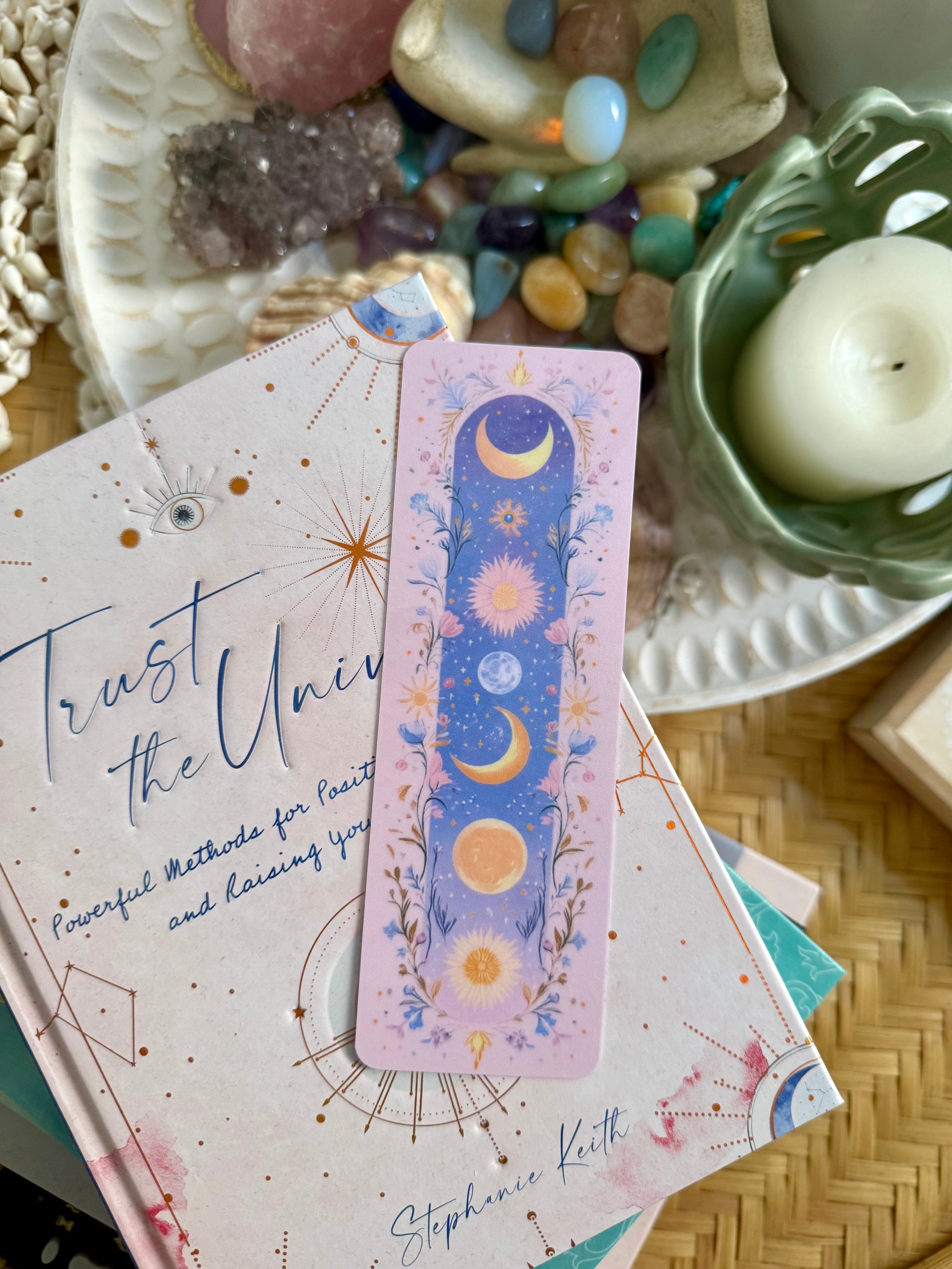 A floral celestial moon bookmark placed on a book with crystals and candles in the background.