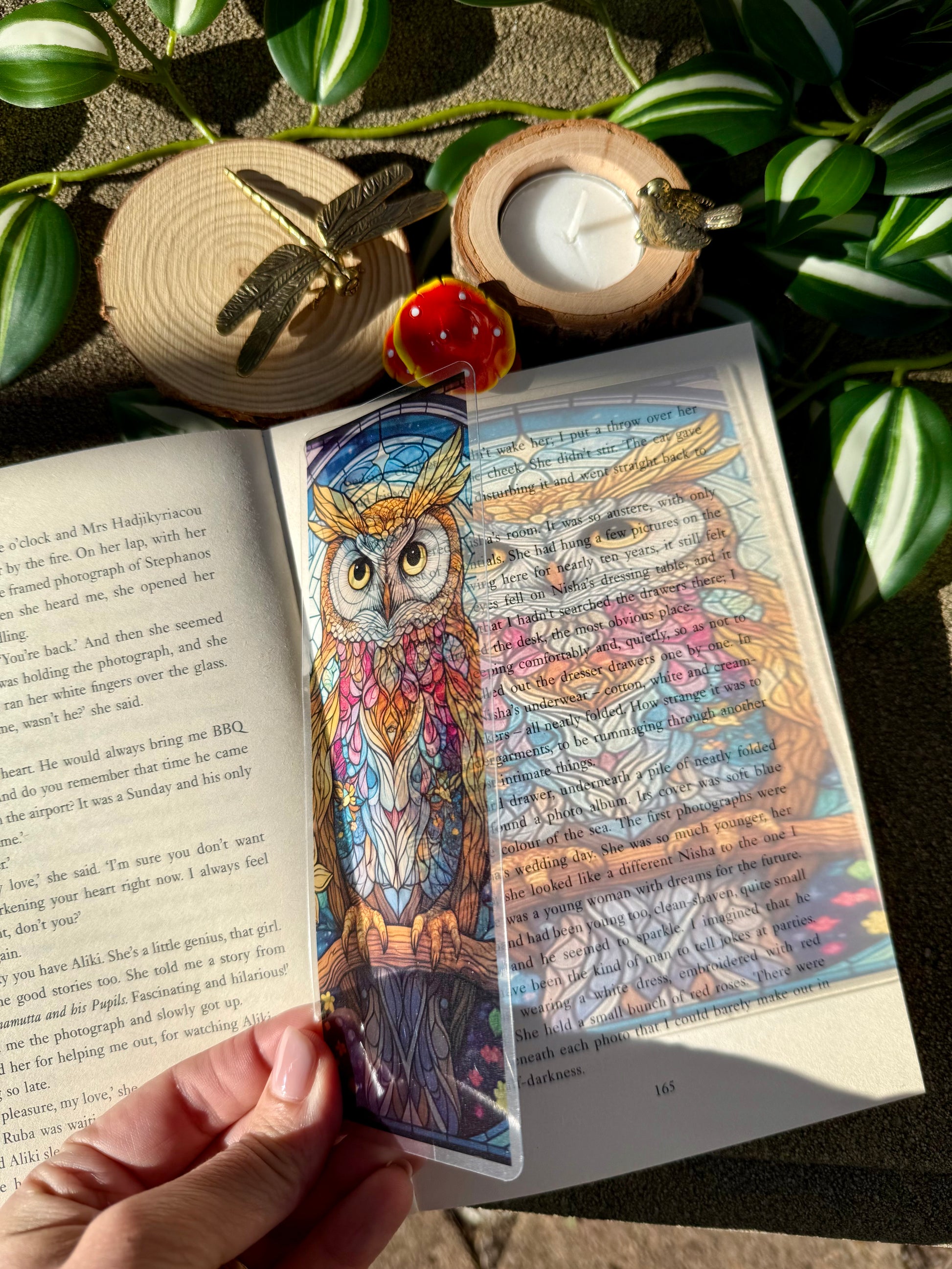 Colorful stained glass owl bookmark held over an open book with the reflection of the bookmark showing on the book