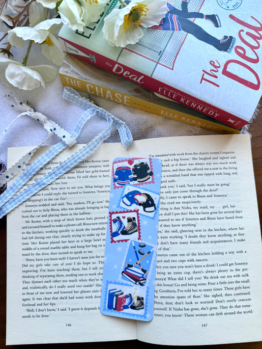 Open book with a bookmark featuring hockey-themed stamps, surrounded by books and flowers.
