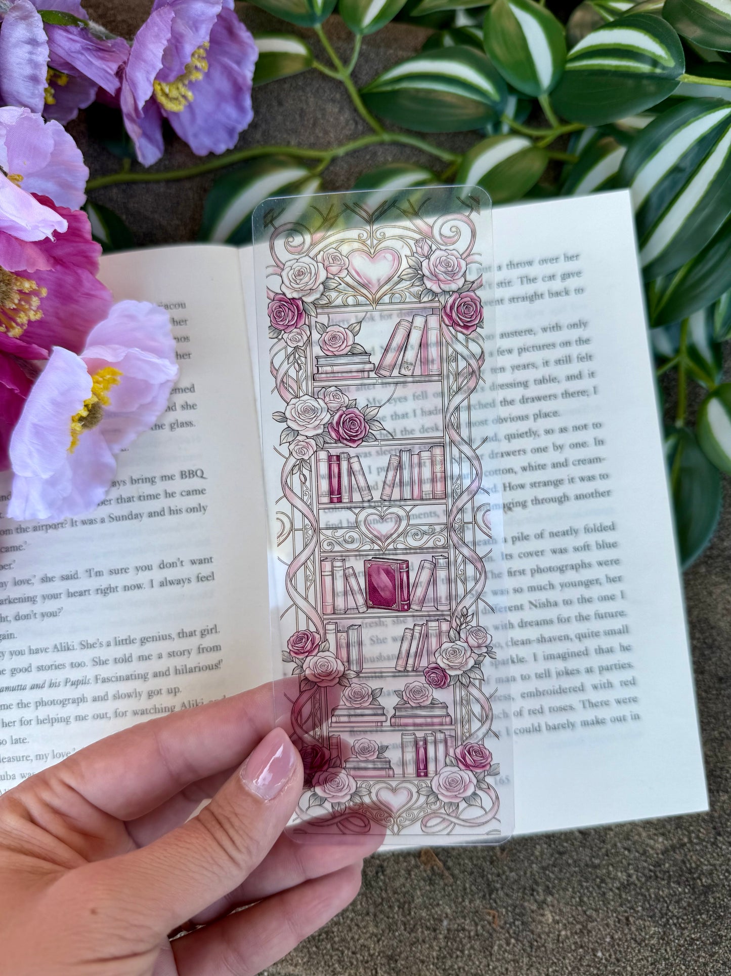 A stained glass bookmark of a book shelf with roses and hearts. The book is placed over an open book.
