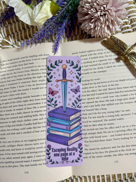 Decorative bookmark with a sword and books design on an open book with flowers and a dragonfly.