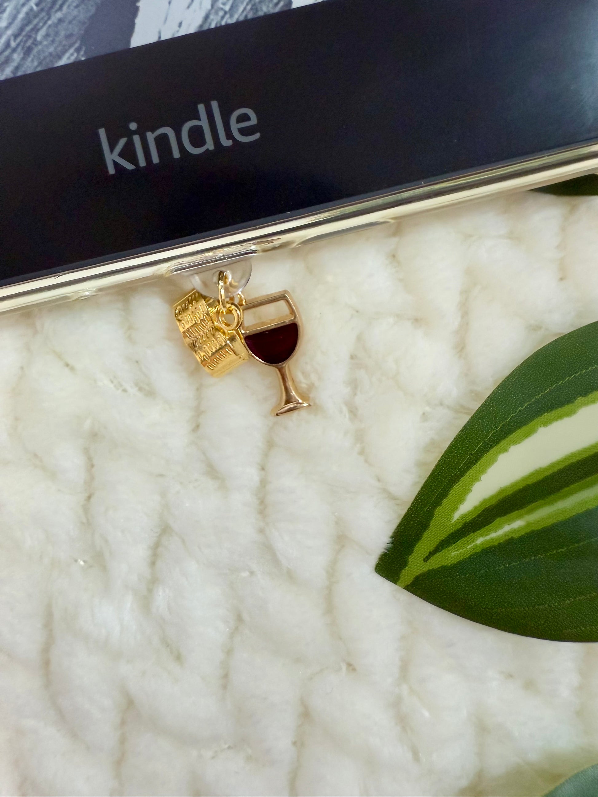 Dust plug with a wine glass and book charm on a Kindle device.
