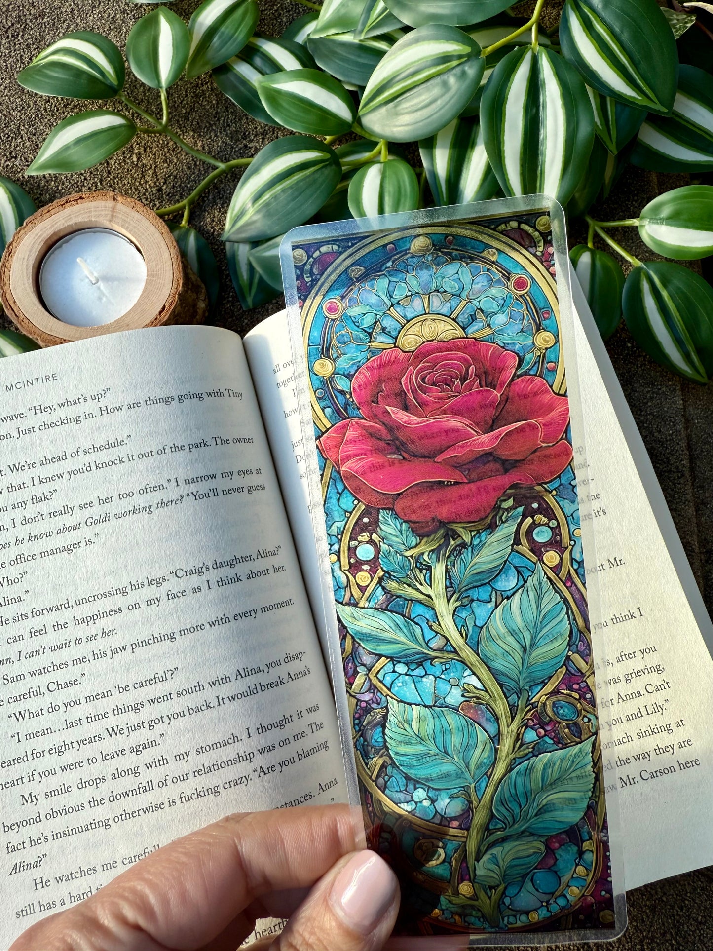 Colorful stained glass-style rose bookmark on an open book with greenery in the background