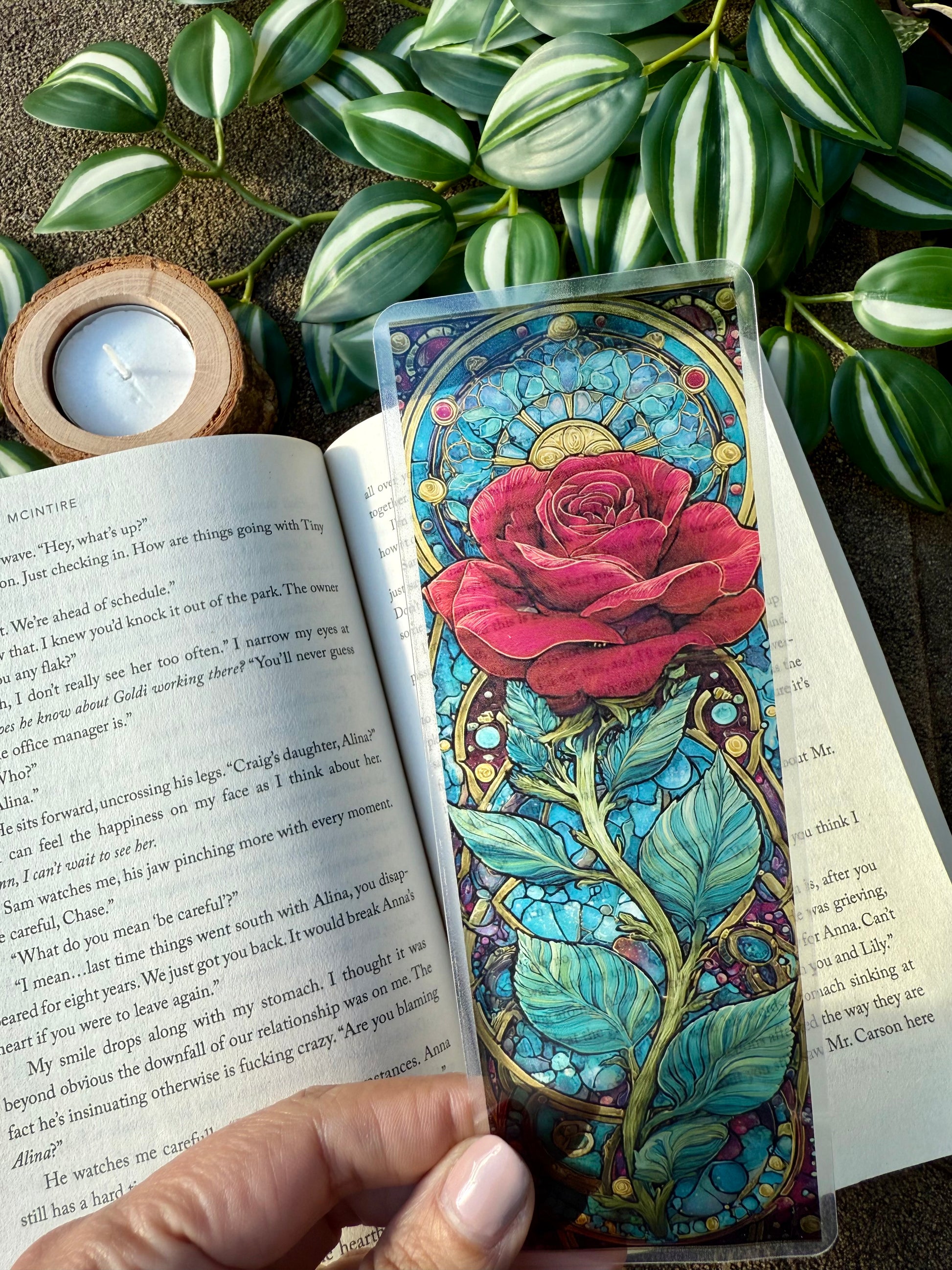 Colorful stained glass-style rose bookmark on an open book with greenery in the background