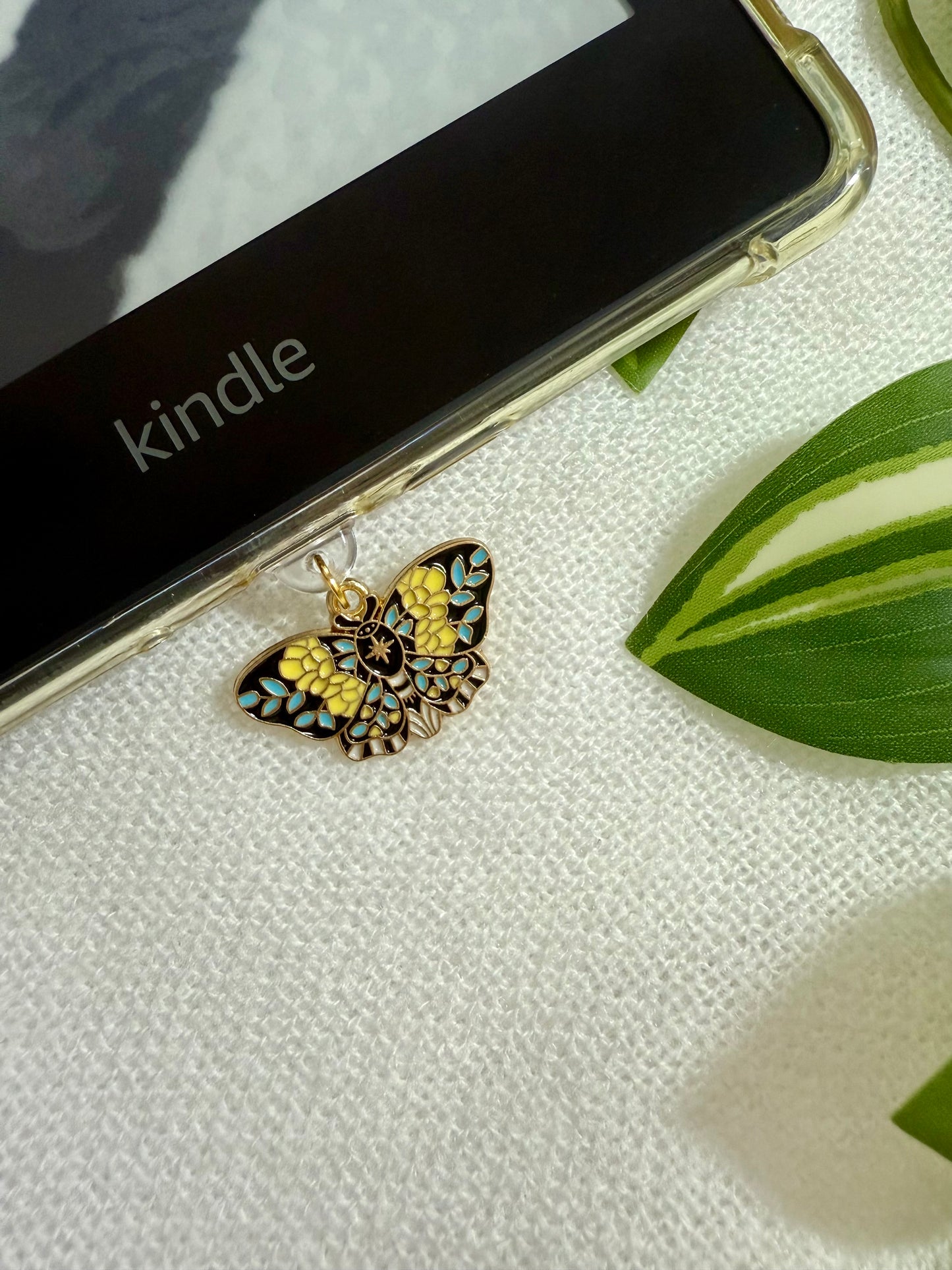 Butterfly-shaped charm on a Kindle device with a leaf in the background