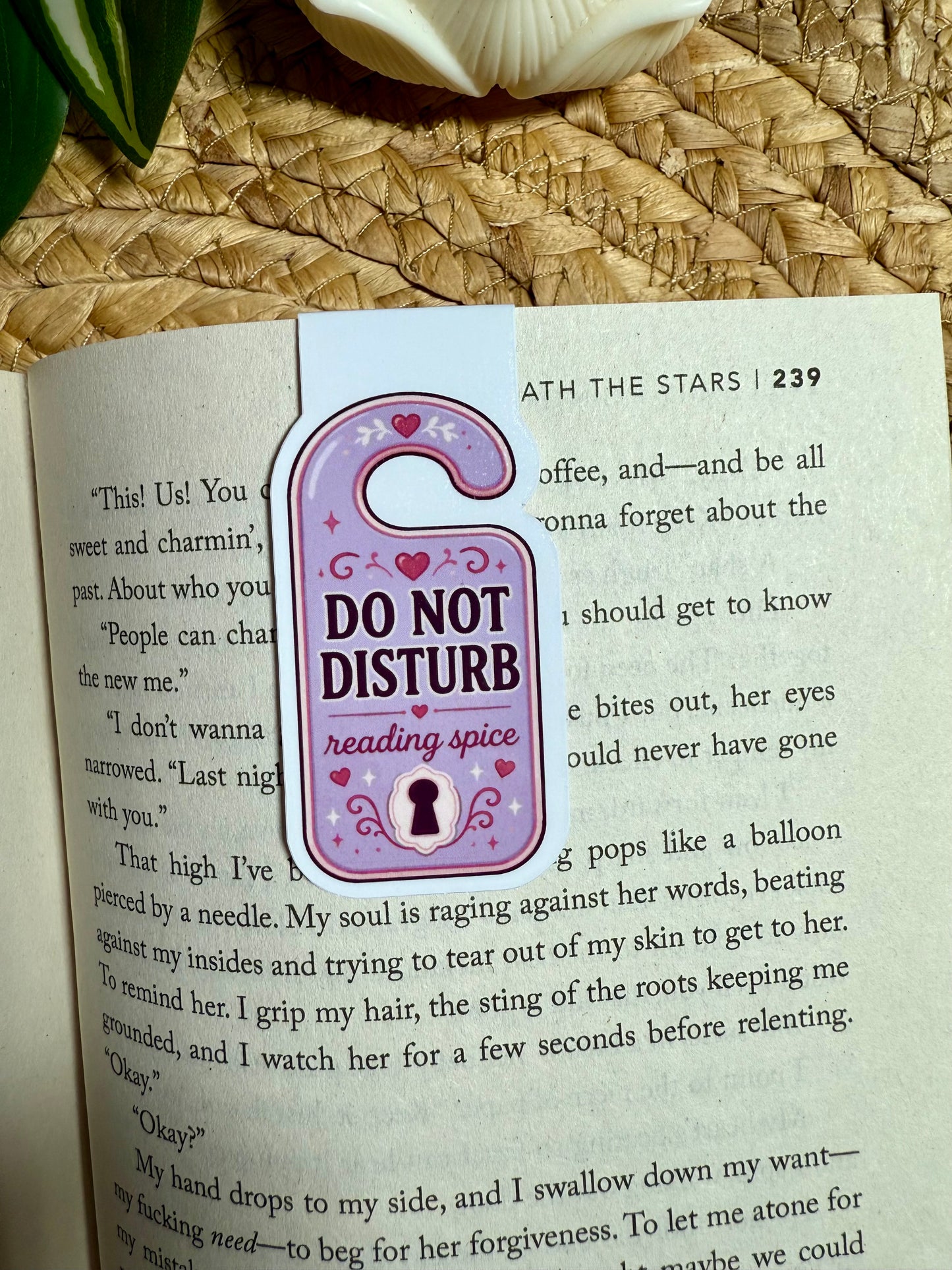 A decorative magnetic bookmark shaped like a hanging doorbell in lavender and pink, printed with the text 'DO NOT DISTURB reading spice,' placed on an open book page.