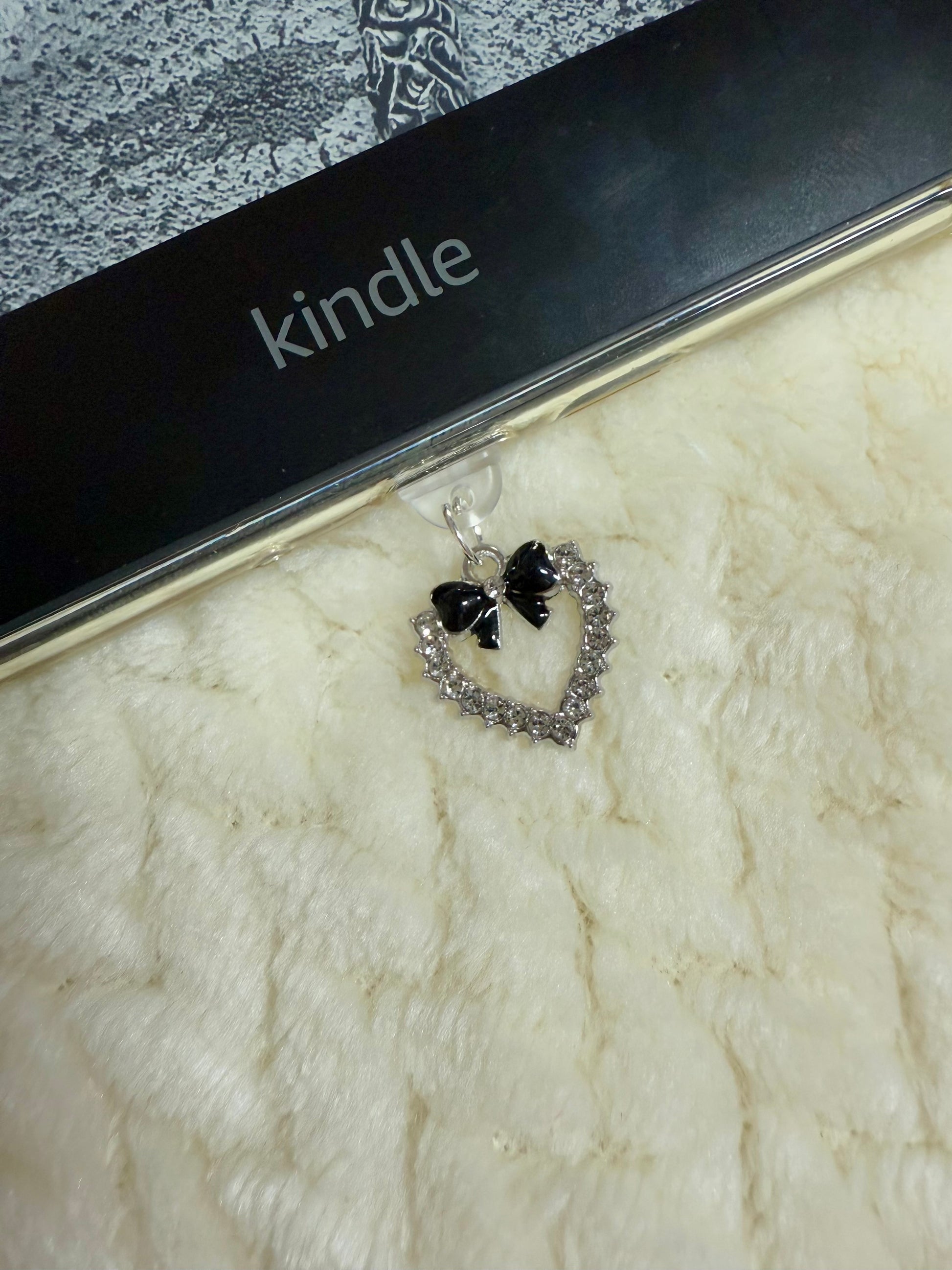 A silver heart with black bow charm attached to a kindle device.