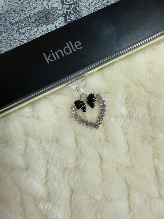 A silver heart with black bow charm attached to a kindle device.
