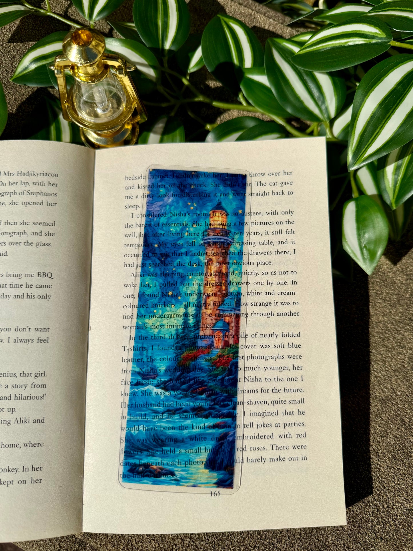 A stained glass bookmark of a lighthouse standing on a cliff edge with the sea below. The bookmark is placed on an open book