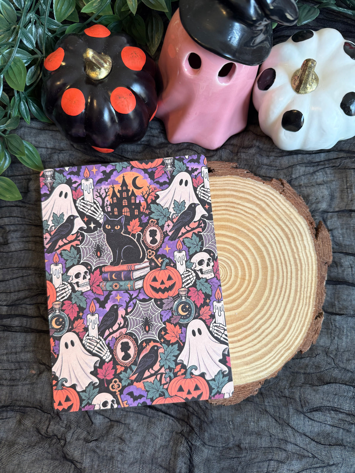 A kindle insert featuring a collage of Halloween inspired images such as ghosts, skulls, black cat, etc. The insert is placed on a wooden block surrounded by Halloween decor.