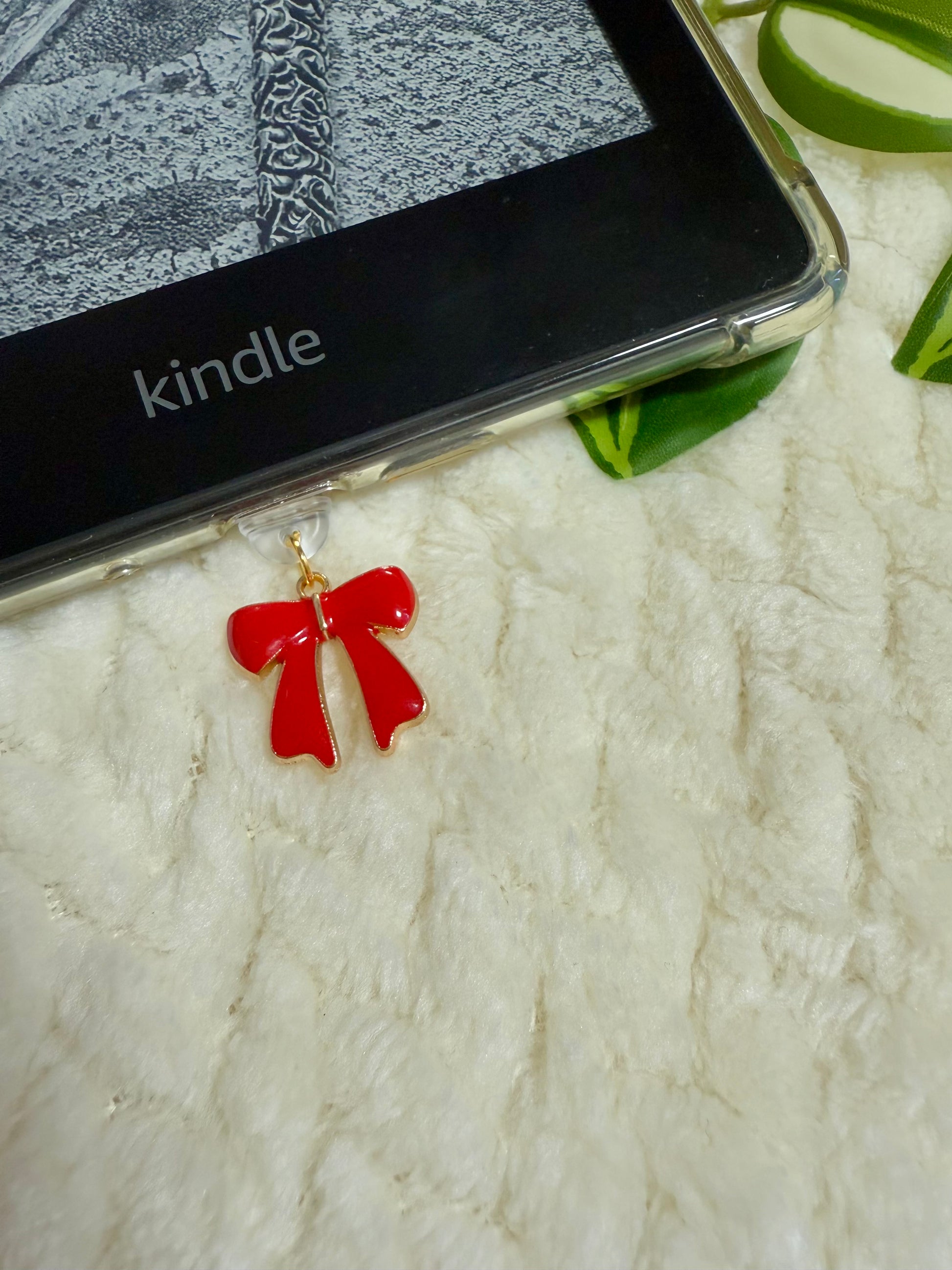 Red bow-shaped charm dust plug on a Kindle device with a white background