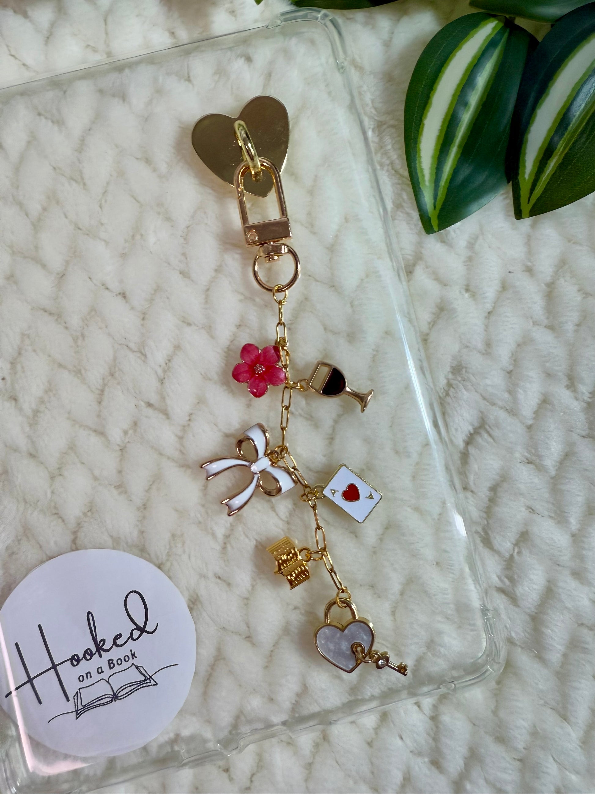 A chain with heart, book, wine, bow charms attached to a clear kindle case.
