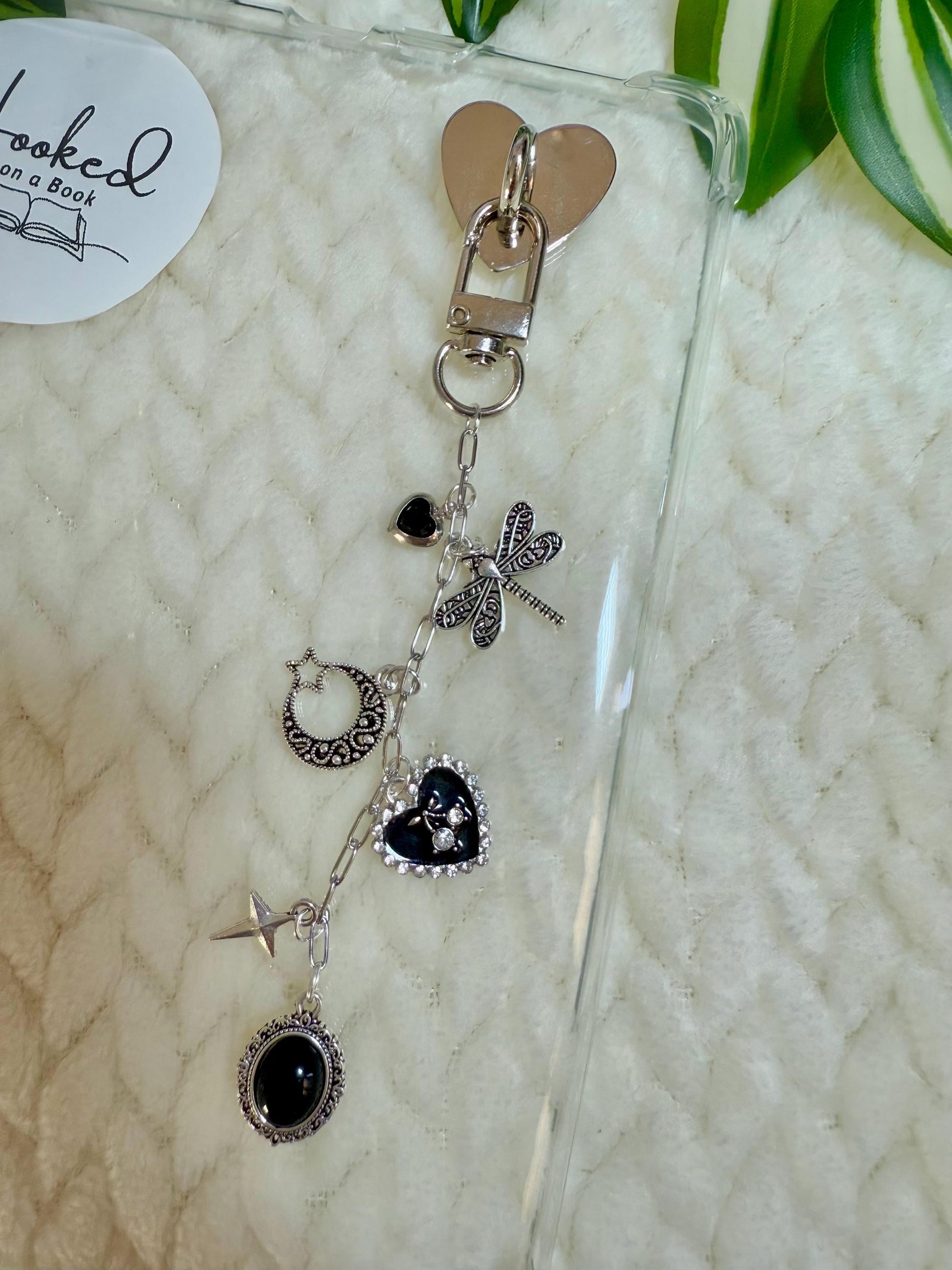 A silver chain with charms such a dragonfly, heart and moon attached to a clear kindle case.
